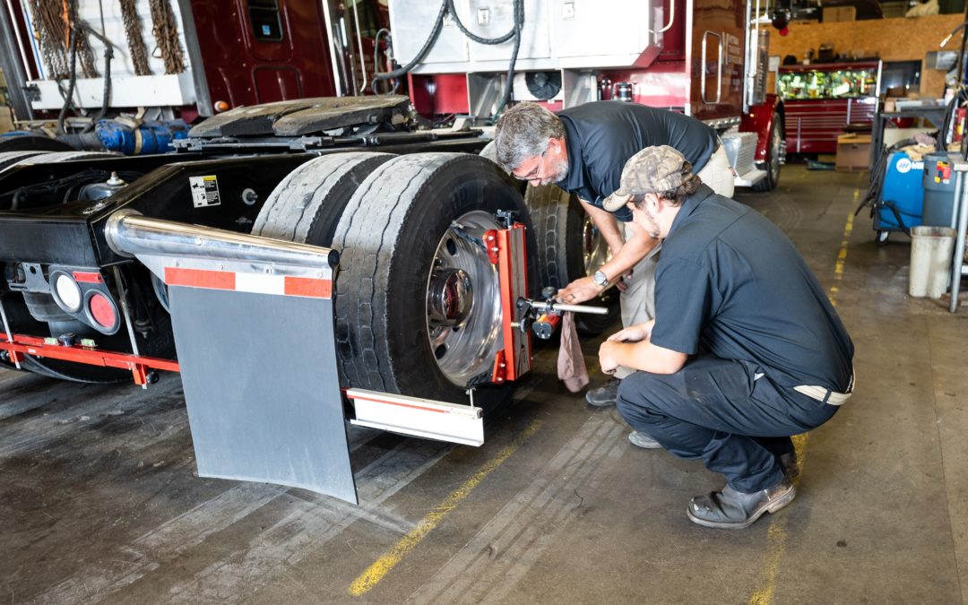 Two certified diesel mechanics checking out the tire of a tractor trailer.