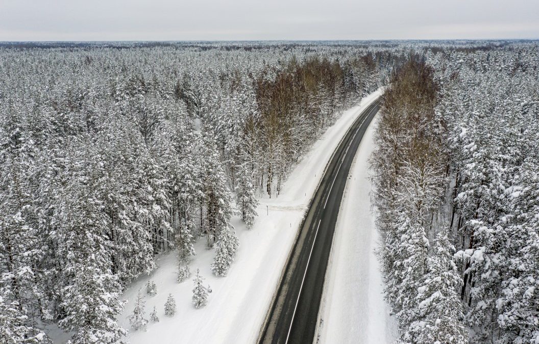 aerial shot of a forest covered in snow with a two lane running through it
